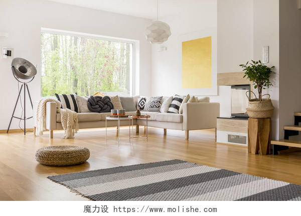 条纹的灰色地毯和编织坐垫凳面板在斯堪的纳维亚风格的客厅里的地板上